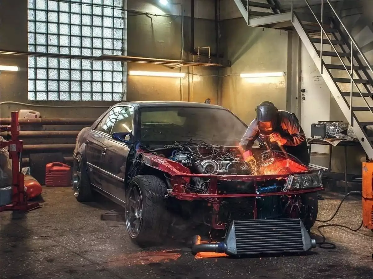 Майстер на СТО проводить зварювальні роботи під капотом авто